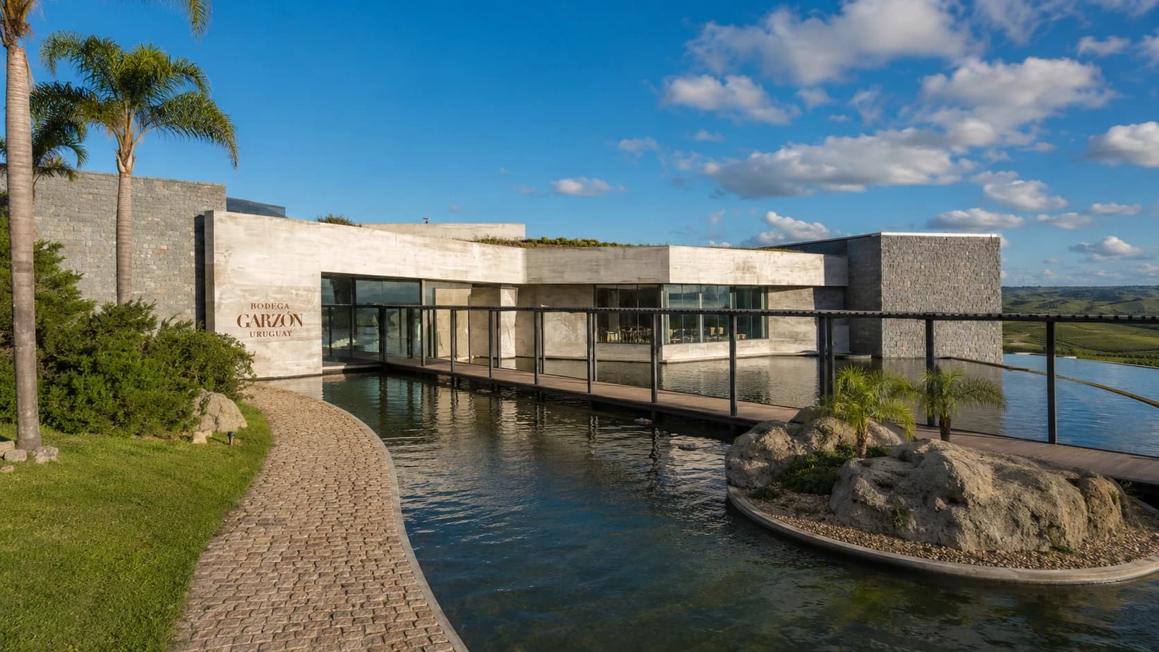 Bodega Garzón entre palmeras, con su espejo de agua y los viñedos de fondo