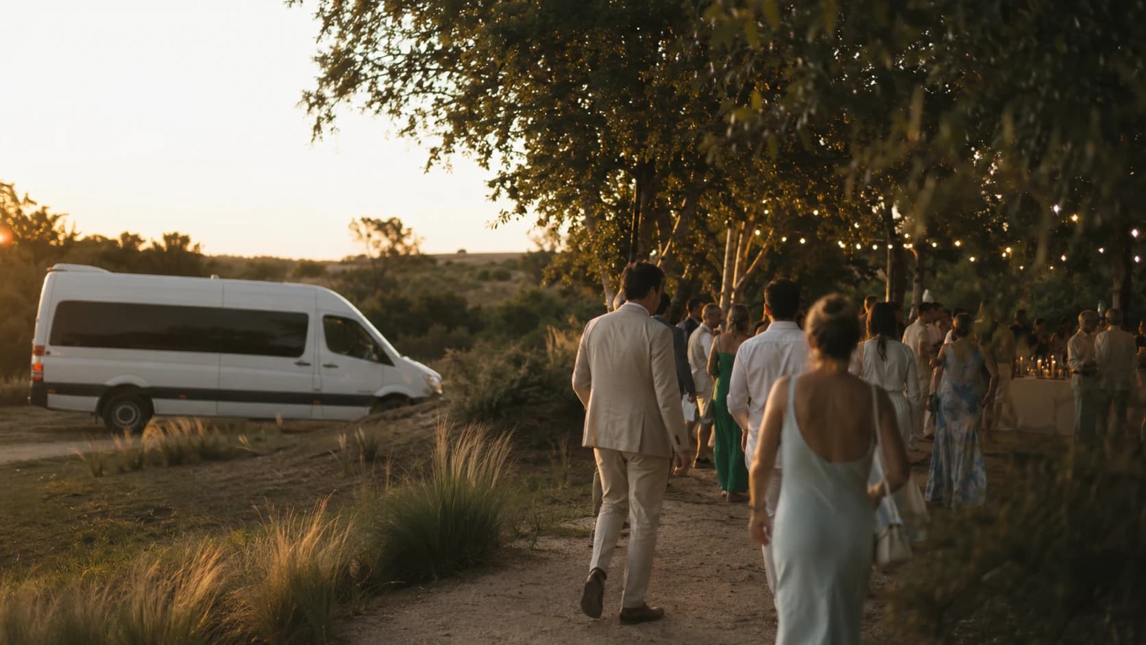 Convidados chegando a um casamento ao entardecer, com a van que os levou estacionada ao lado do caminho